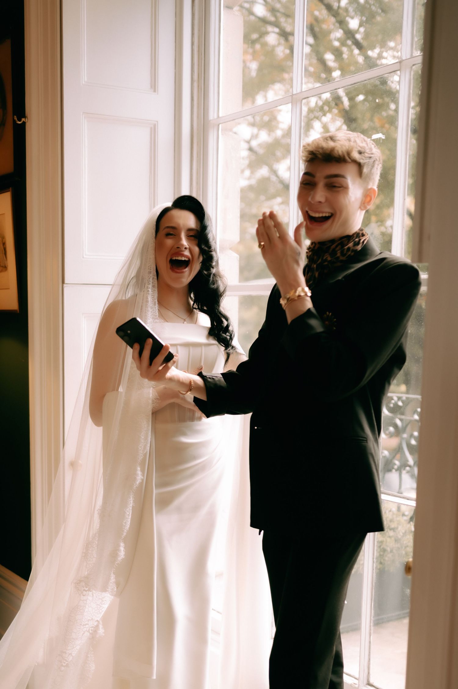 A joyful couple shares a candid moment dancing together by sunlit windows during their wedding celebration.