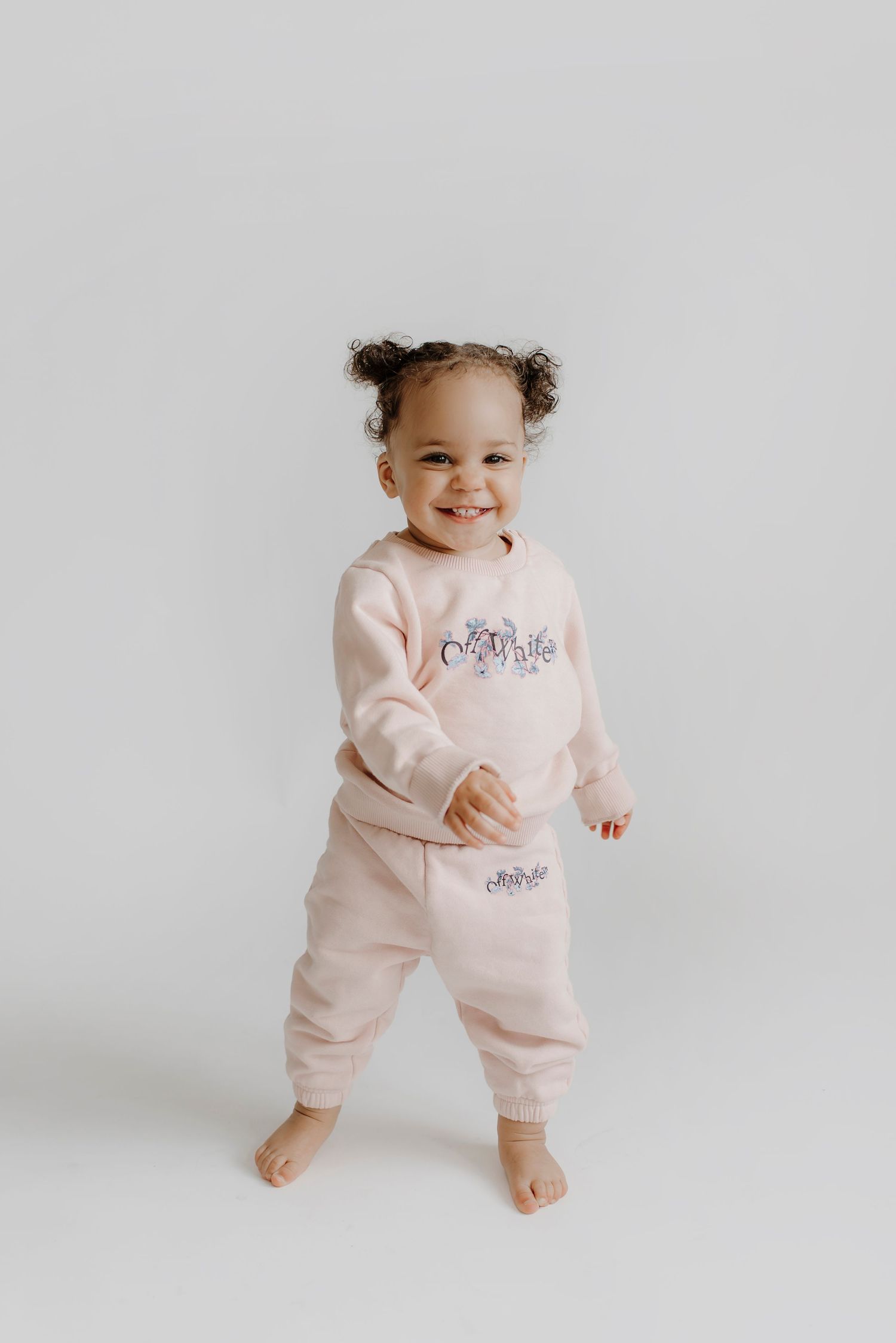 Baby wearing pink outfit against white background in studio setting.