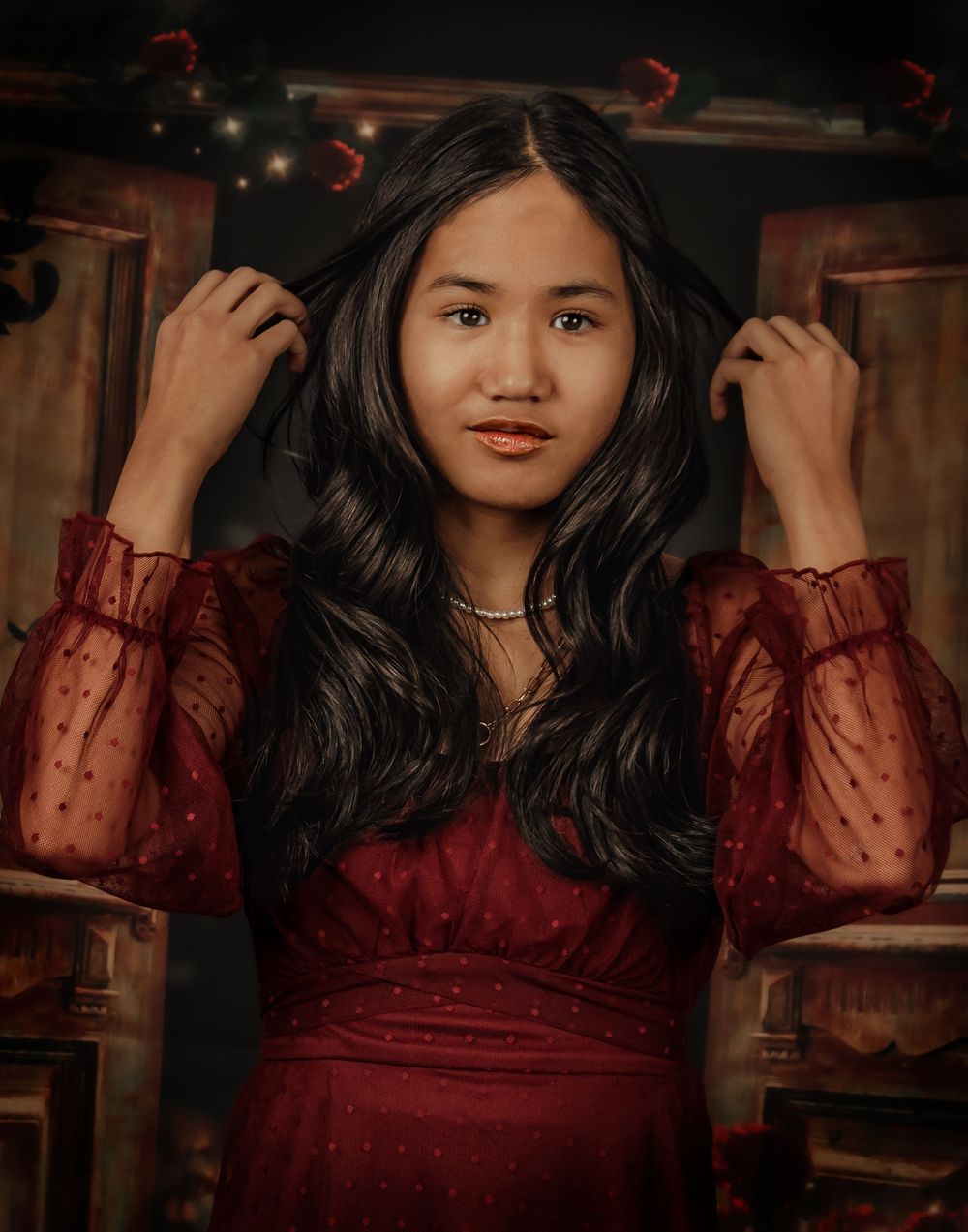 Dark and romantic portrait featuring sheer long sleeves and deep red dress against vintage backdrop.