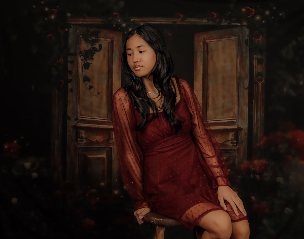 A person in a burgundy dress poses against a dark rustic backdrop in a moody portrait series.