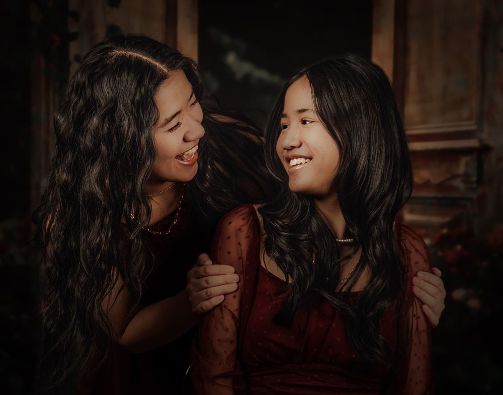 Two people share an intimate moment while smiling and laughing together in a dimly lit setting.