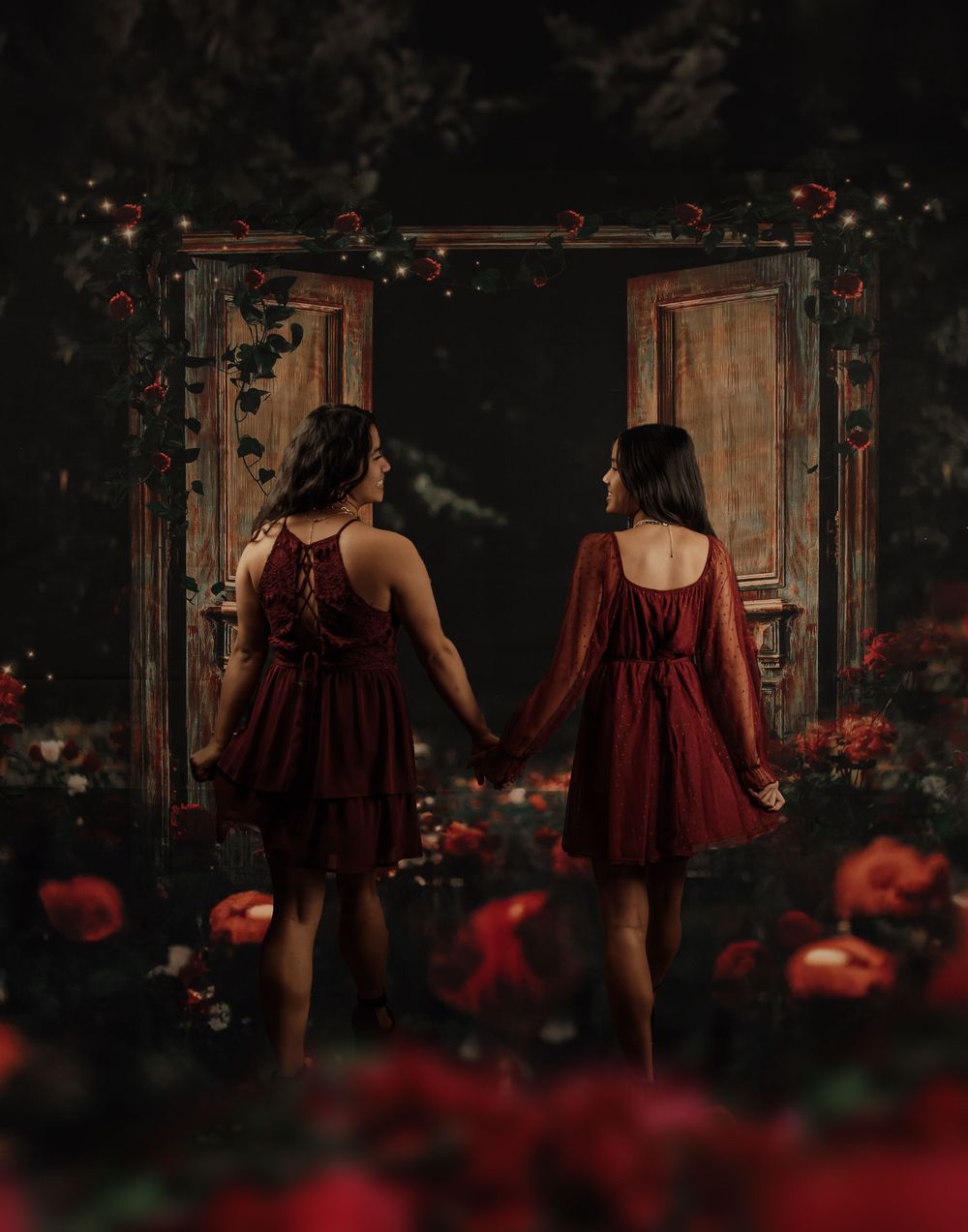 Two matching burgundy dresses shown in dramatic dark photoshoot with red flowers.