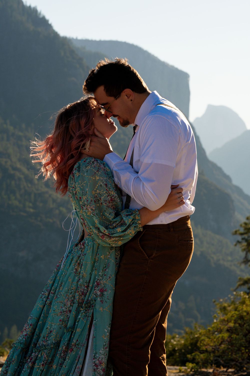 Elopement couple in romantic embrace dances against a backdrop of majestic granite mountain cliffs during golden hour sunset. Yosemite CA