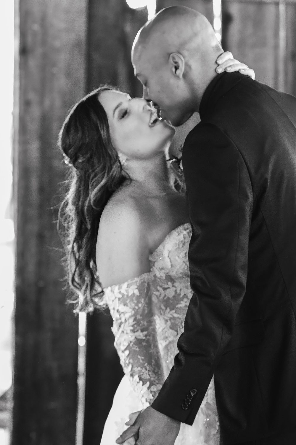 A romantic black & white wedding photo showing a couple sharing intimate kisses in formal attire at their rustic barn wedding, Mendocino, Ca