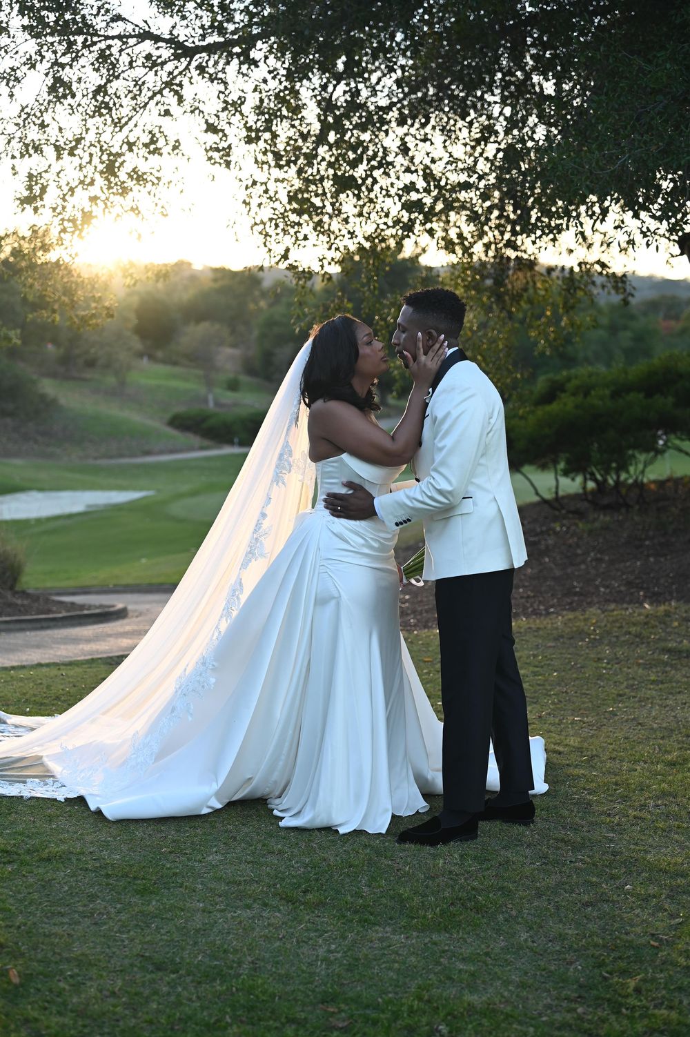 A romantic wedding couple shares a tender moment at sunset on a golf course with a flowing white veil and dress. Wine Country - Napa, CA