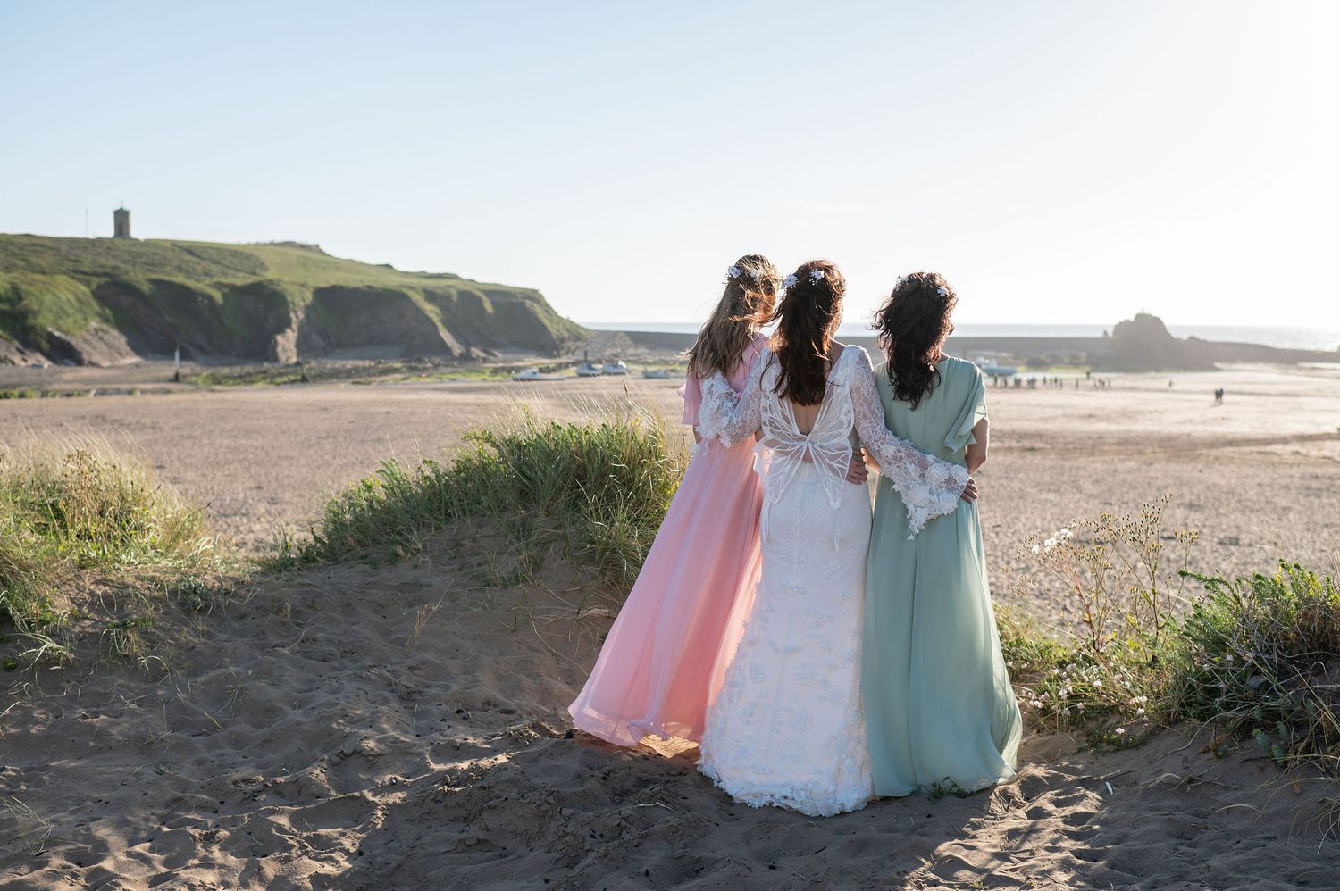 Bride and two bridesmaids stand on Bude beach looking out to sea