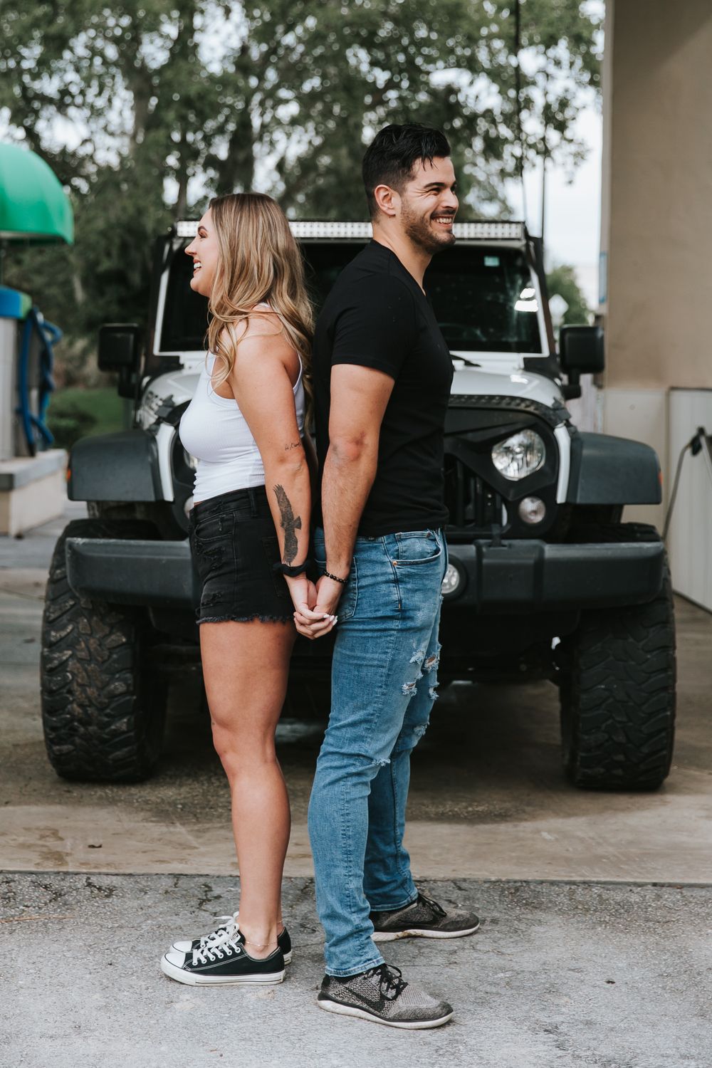 Couple standing together in casual attire with a black vehicle visible in the background.