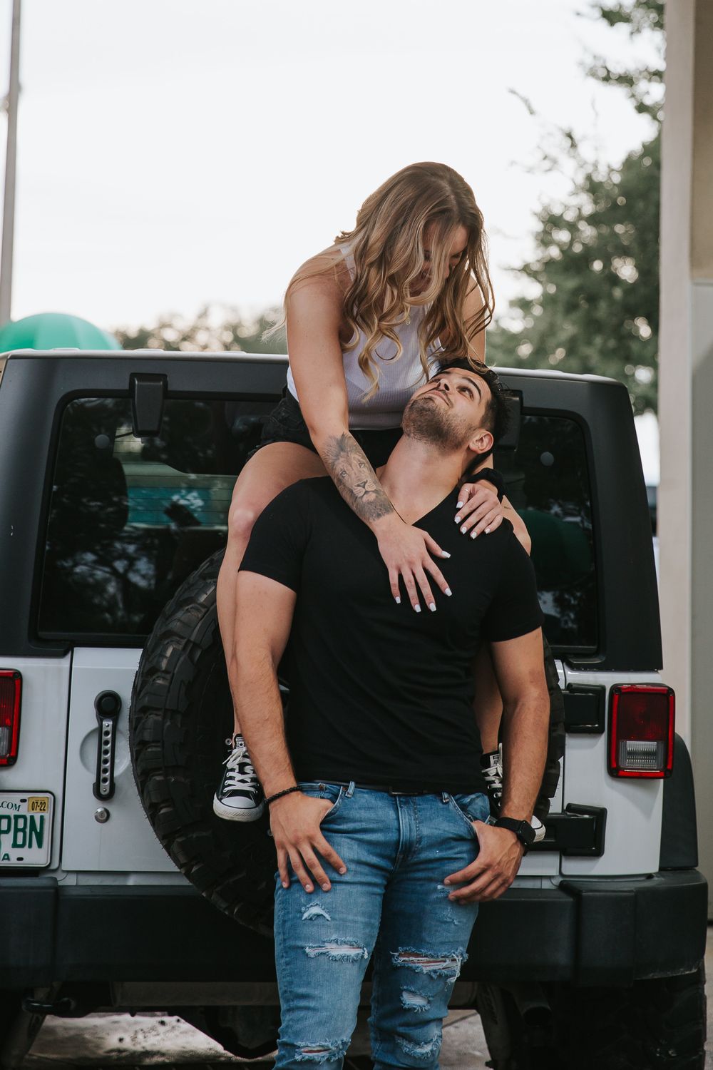 A couple embraces next to a black vehicle in an outdoor setting.