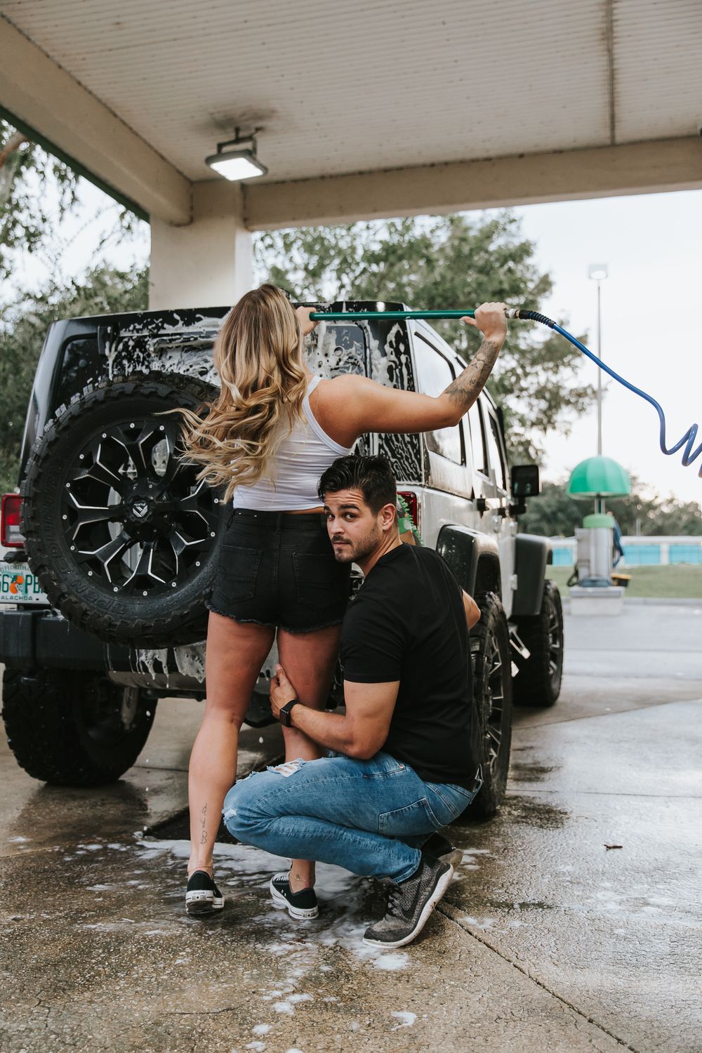 Couple having fun while washing and scrubbing their black off-road vehicle together.