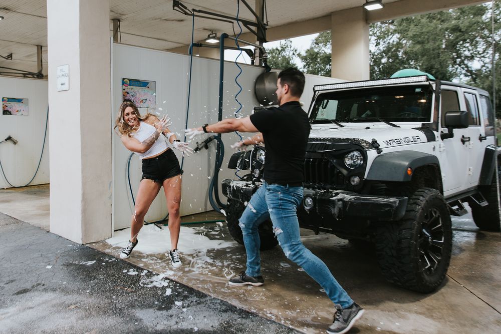 A couple shares a romantic moment while washing their black Jeep at a self-service car wash bay.