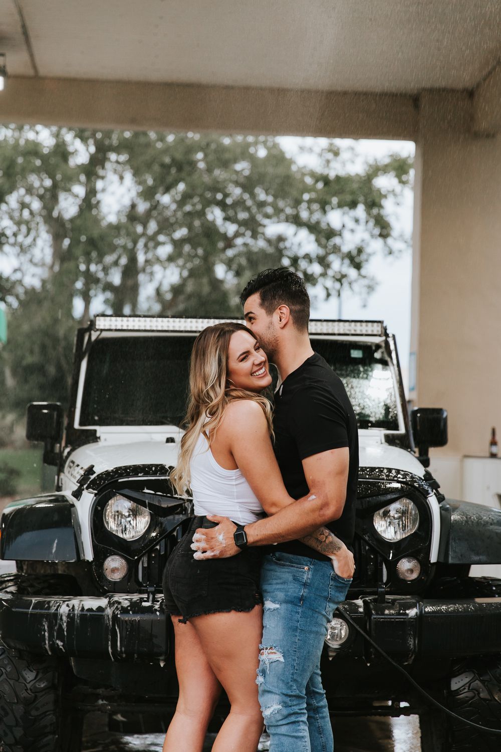 A romantic couple embraces in front of a black Jeep Wrangler in a monochrome photoshoot series.