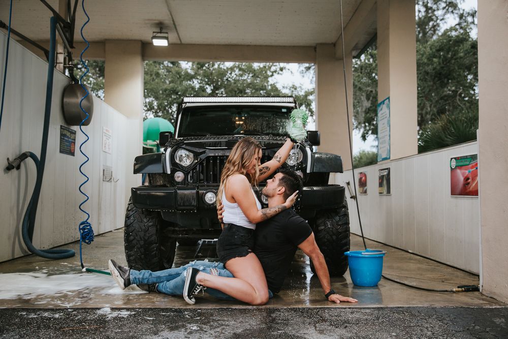 A couple having fun and getting wet while washing their vehicle at an outdoor car wash station.