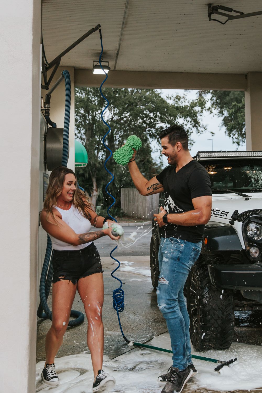 Playful car wash scene with water spraying and laughter under a covered parking area.