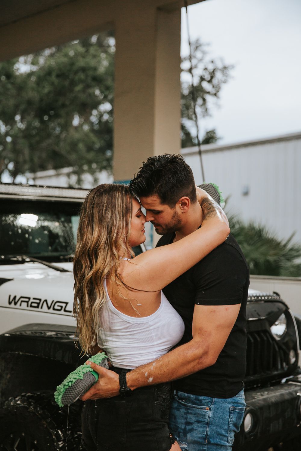 Romantic moment between couple during an outdoor car wash session next to their Jeep.