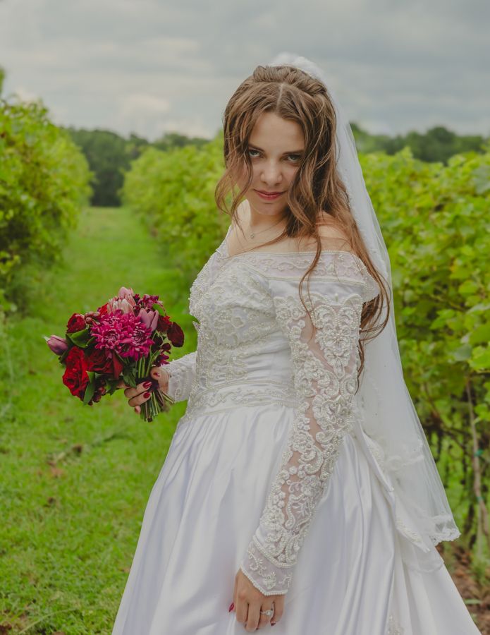 bride in a vineyard holding a bouquet wearing a white dress.