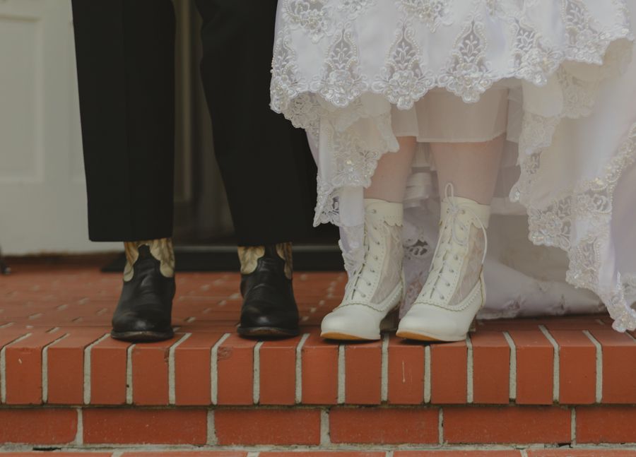 husbands cowboy boots and wifes elegant lace boots. wife lifting dress to reveal shoes. Wedding photography.