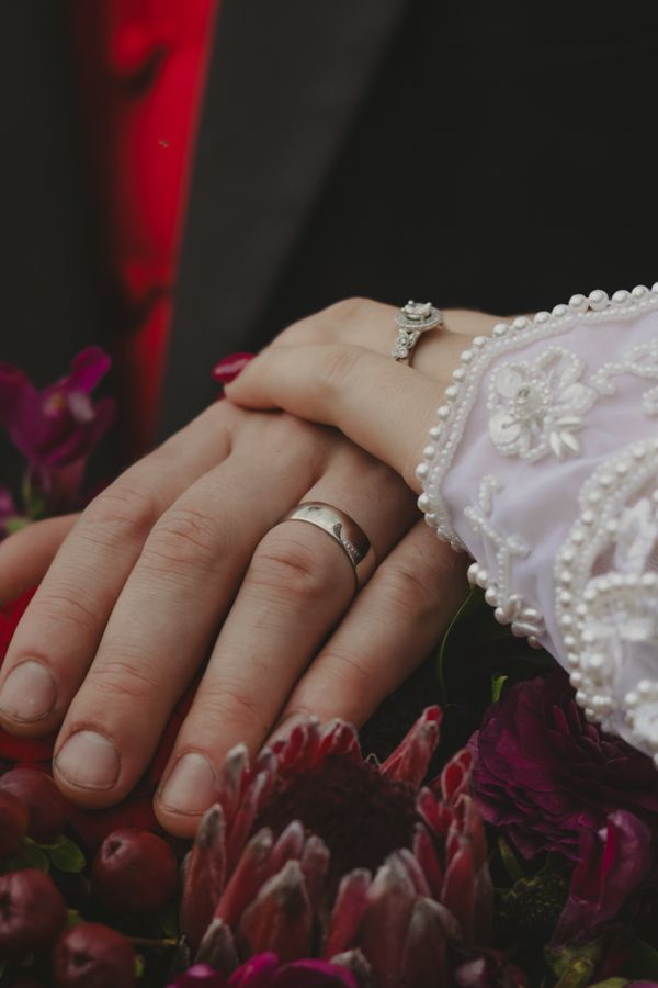 husband and wife wedding rings on wine colored flowers. wedding photographer.