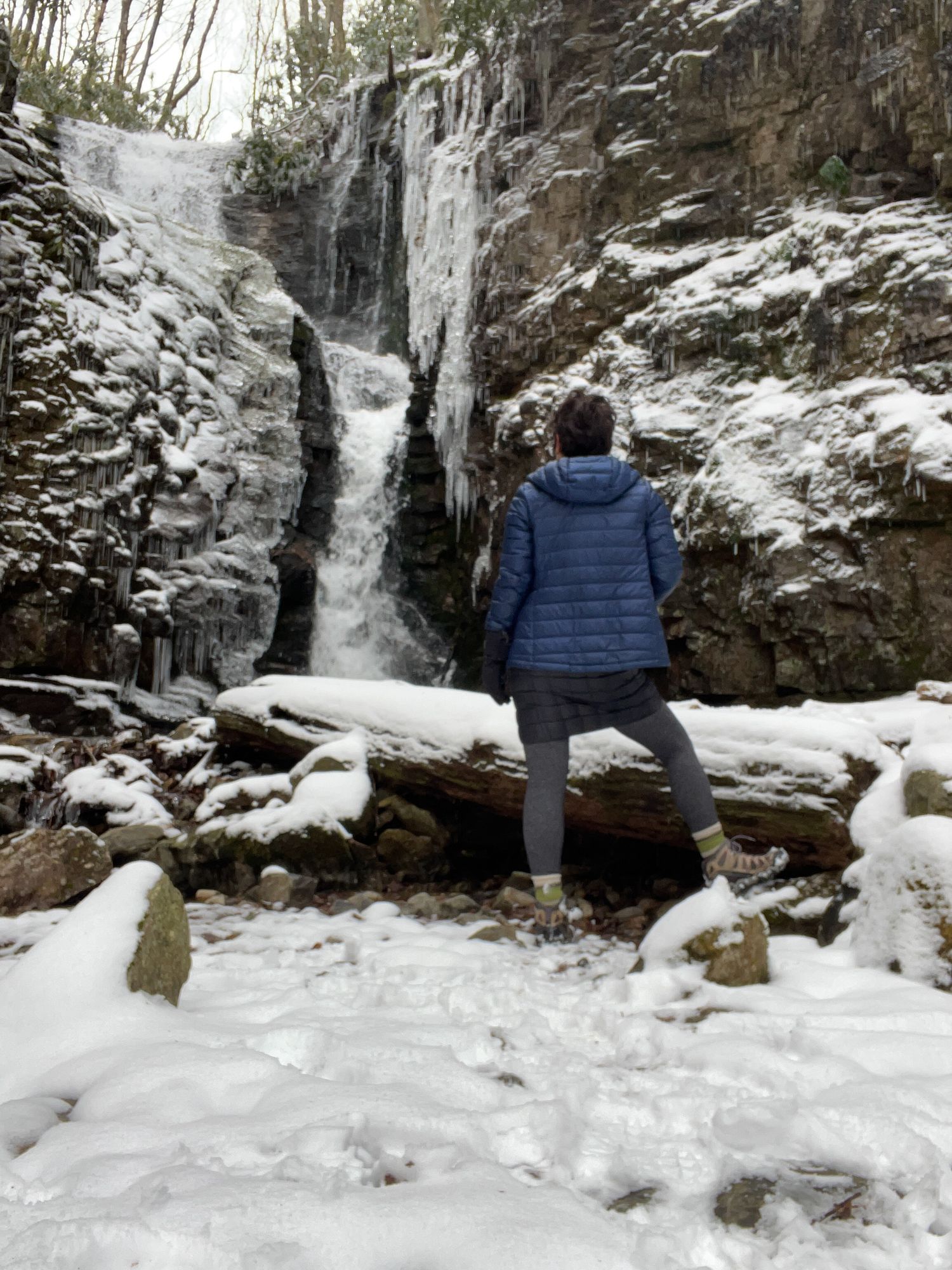 A woman stands looking at a frozen waterfall after a winter hike in Eastern Tennessee