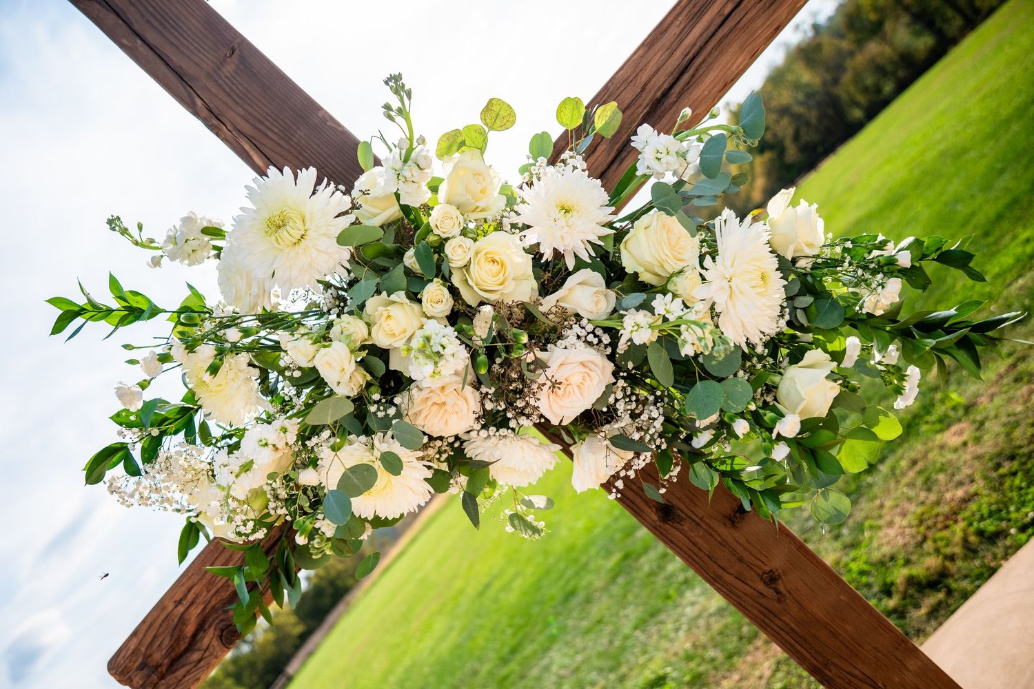 White floral wedding arch decorations against green outdoor setting.
