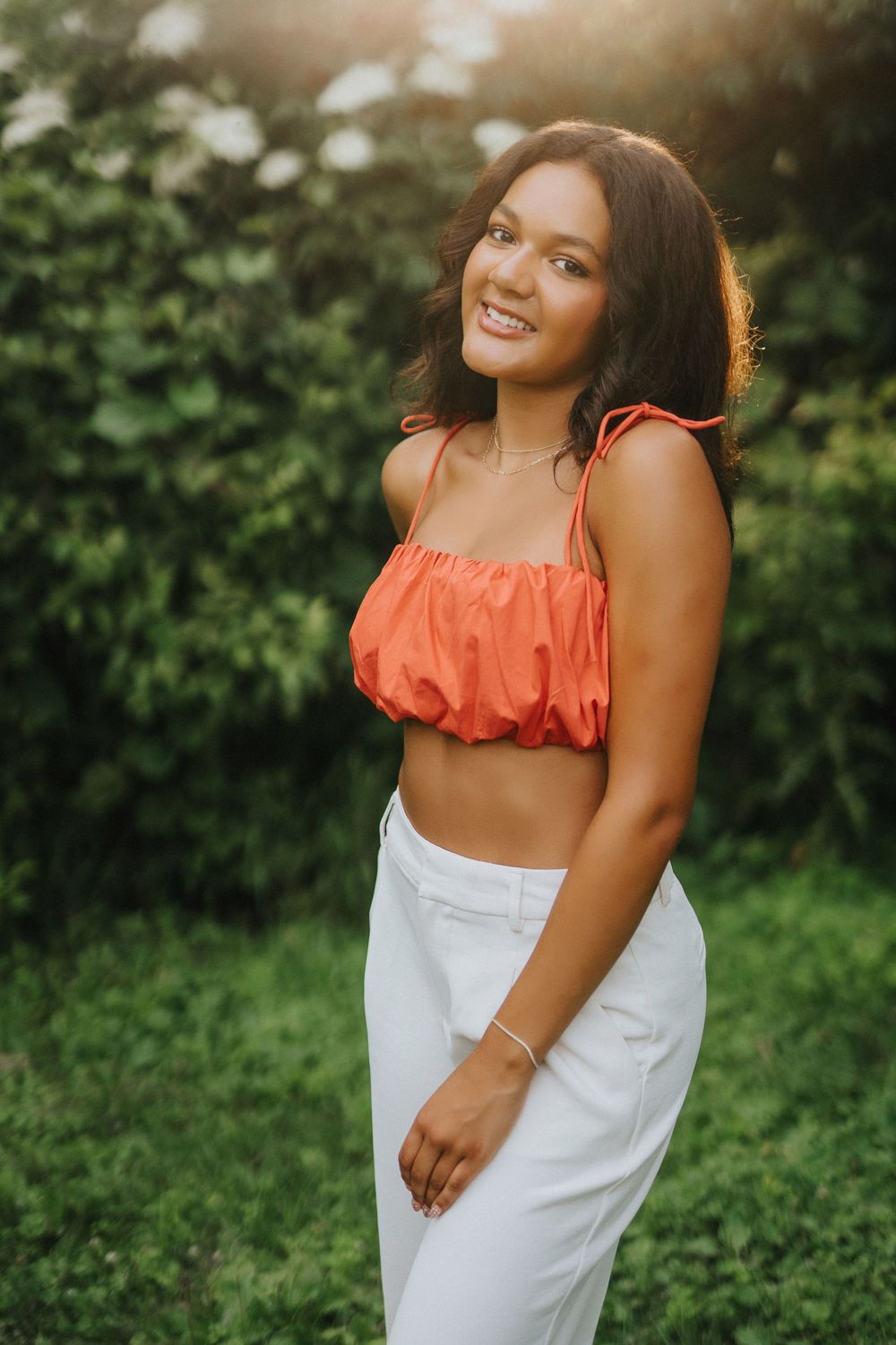 Candid outdoor photo series featuring warm smiles and poses in a white dress with orange accents amid greenery.