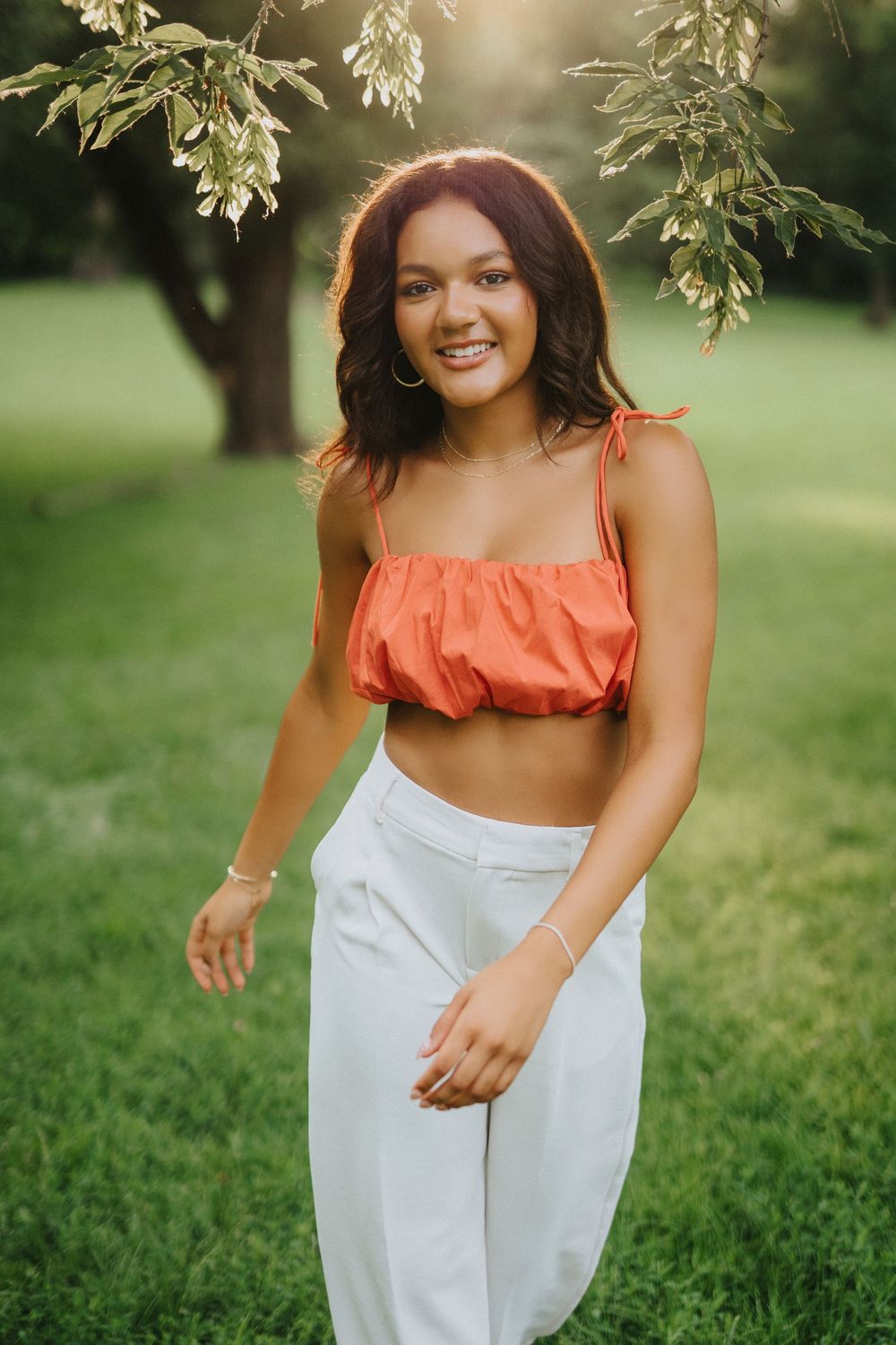 A summer portrait in a park featuring a coral crop top and white pants against a green natural background.
