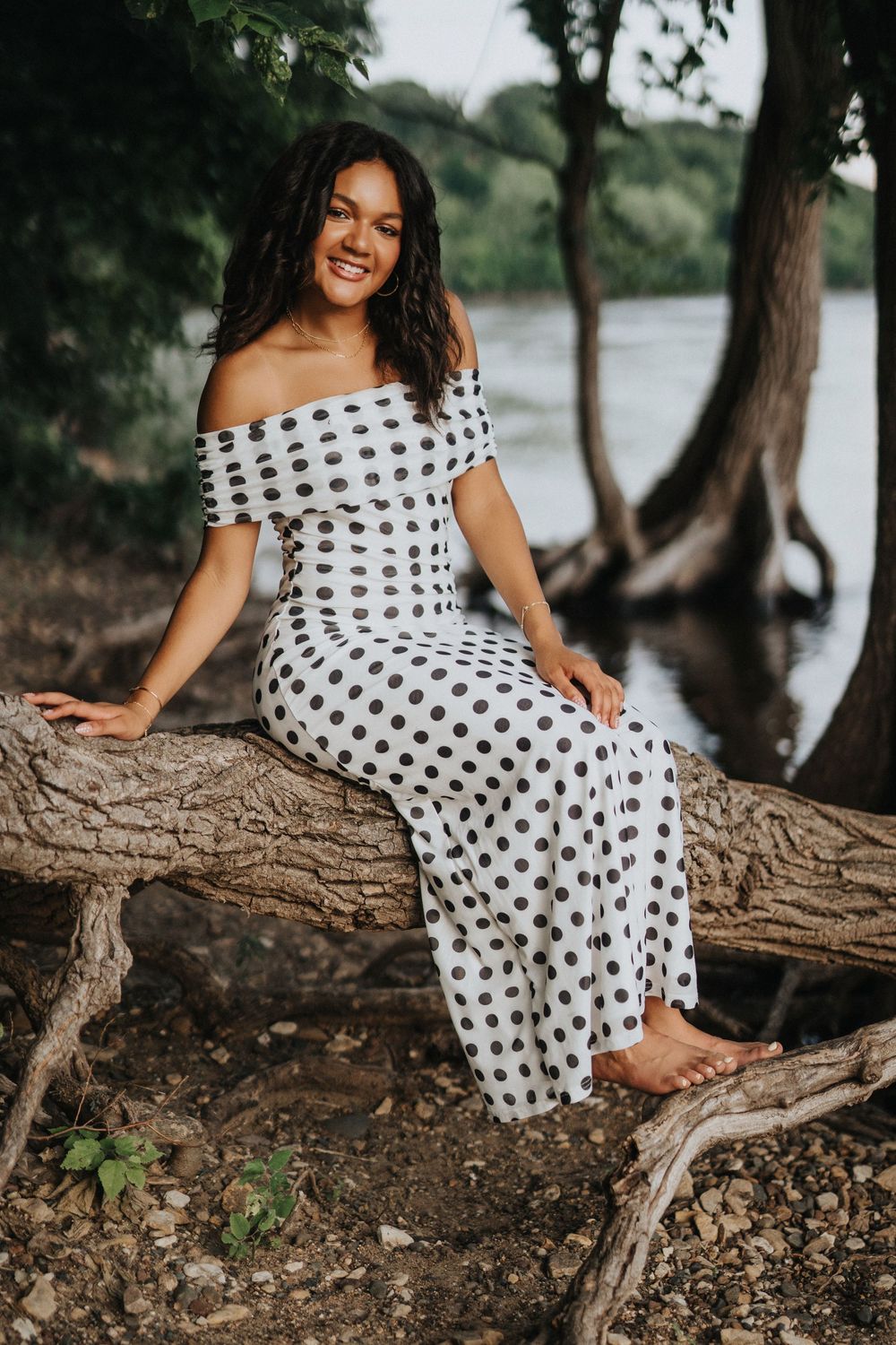 A polka dot off-shoulder dress worn while sitting on a fallen tree trunk by a lake in a natural setting.