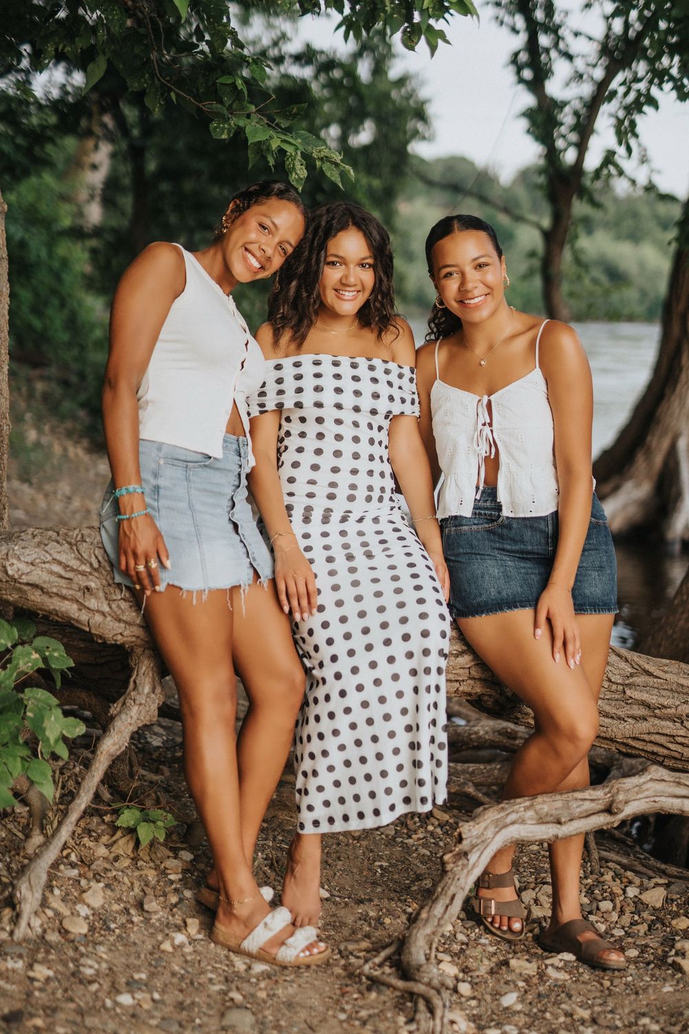 Friends sit together on a fallen tree trunk by the water's edge on a sunny summer day.