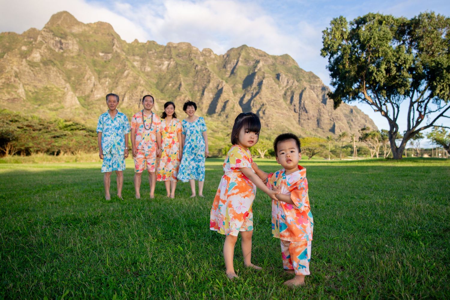 People in colorful floral outfits pose for photos in a scenic mountain landscape at Kualoa.