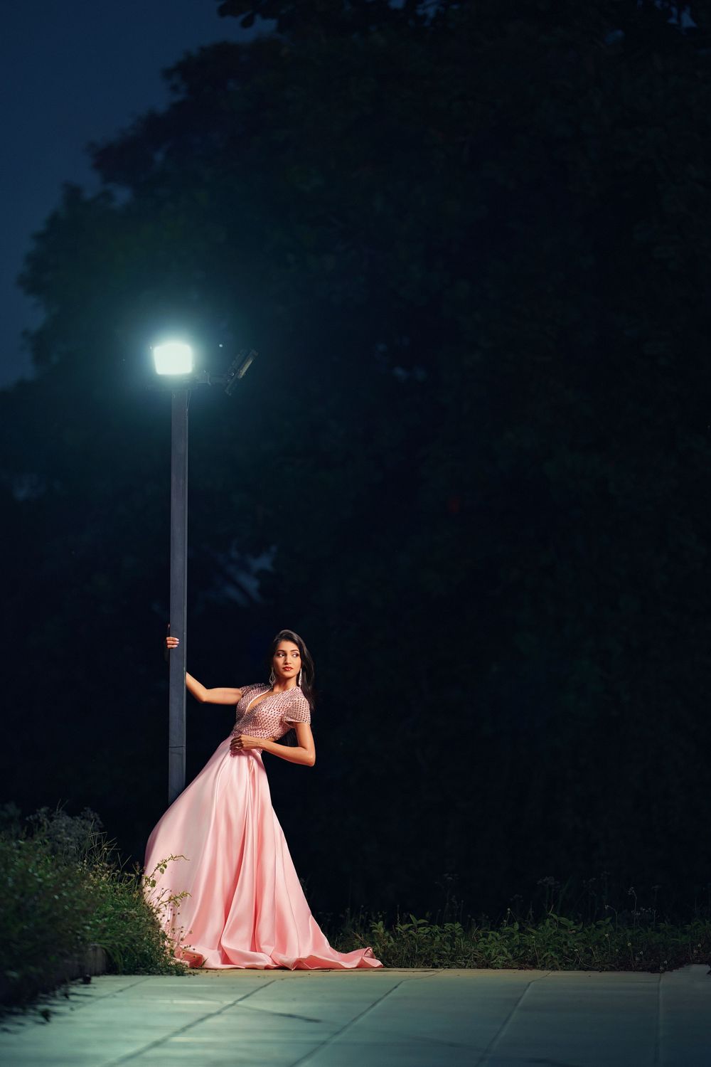 A figure in a flowing pink gown poses dramatically under a street lamp at night in a series of artistic shots.