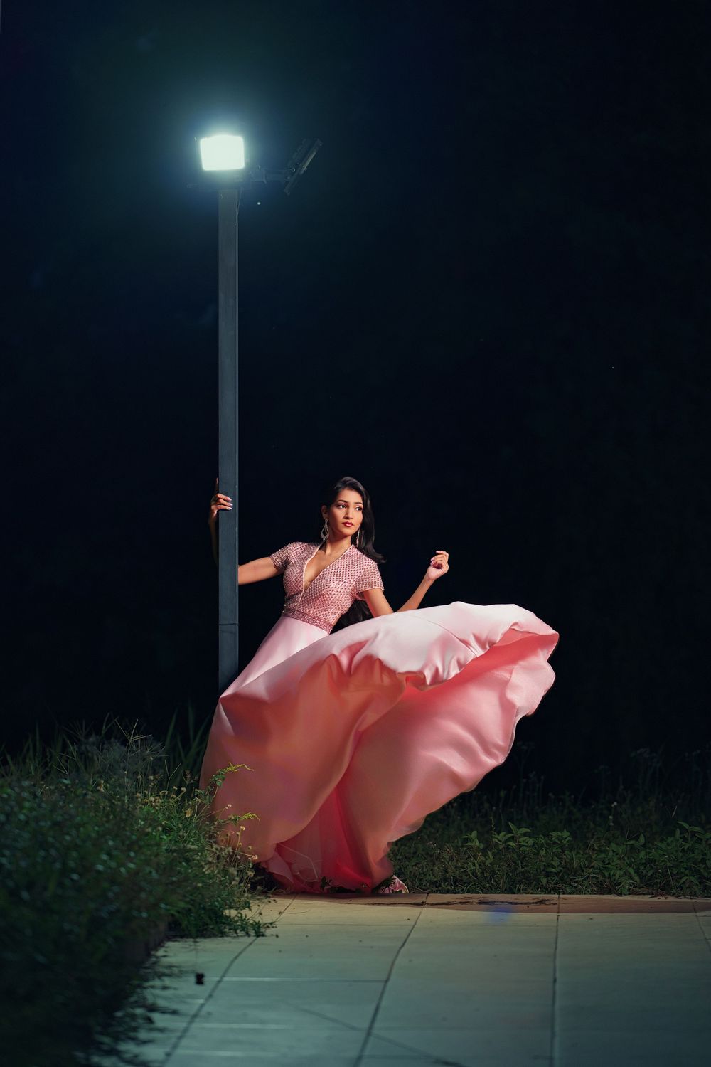 A flowing pink dress billows dramatically under a streetlight at night in a series of dance-like movements.