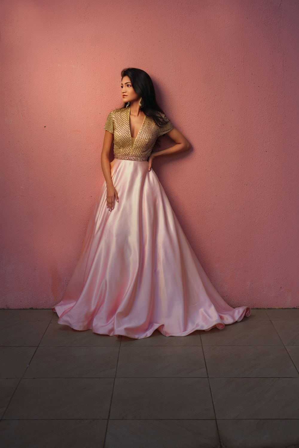 A flowing pink and gold gown is showcased in a series of dramatic poses against a pink wall.
