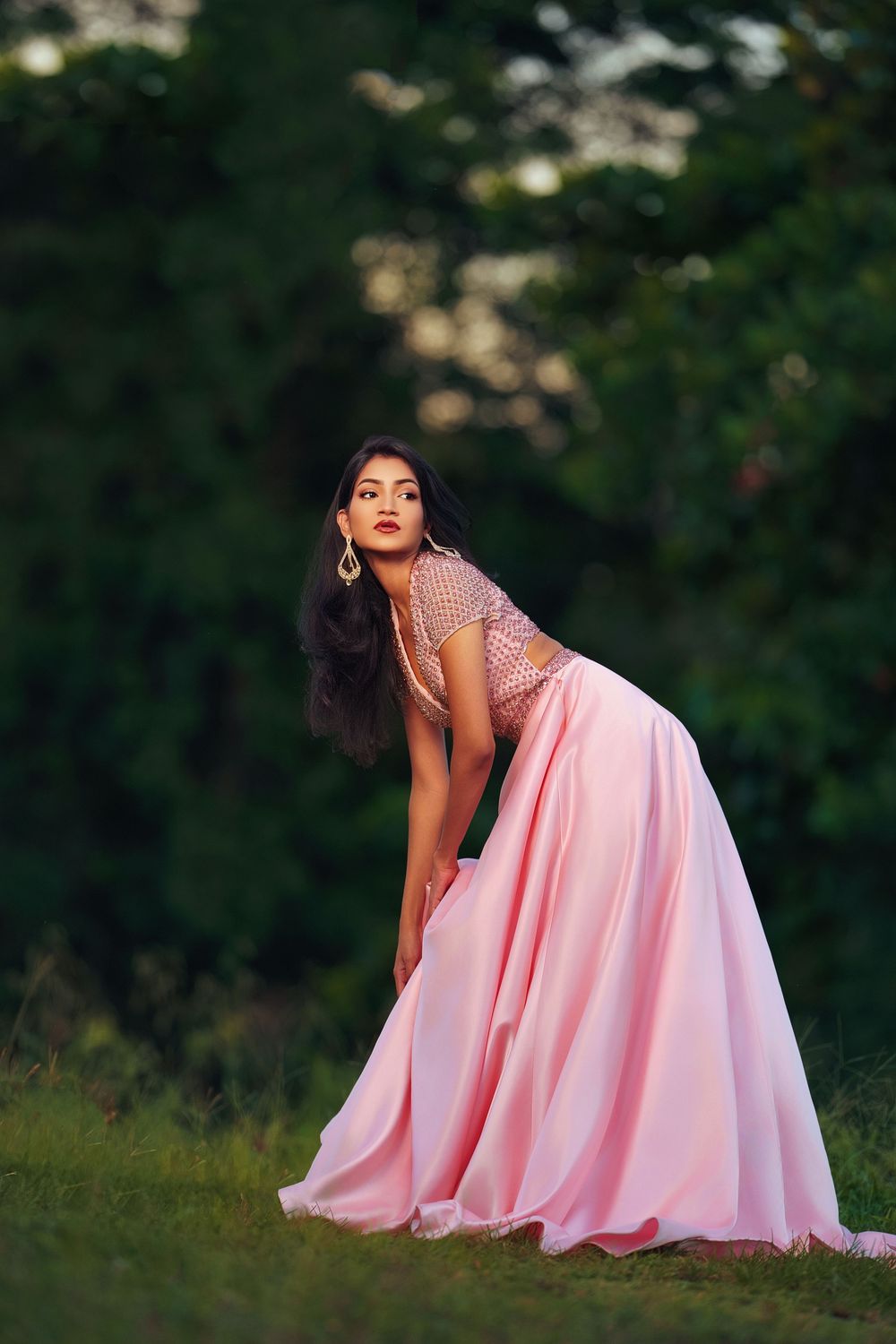 A pink gown flows gracefully against a backdrop of green foliage in an outdoor photoshoot.