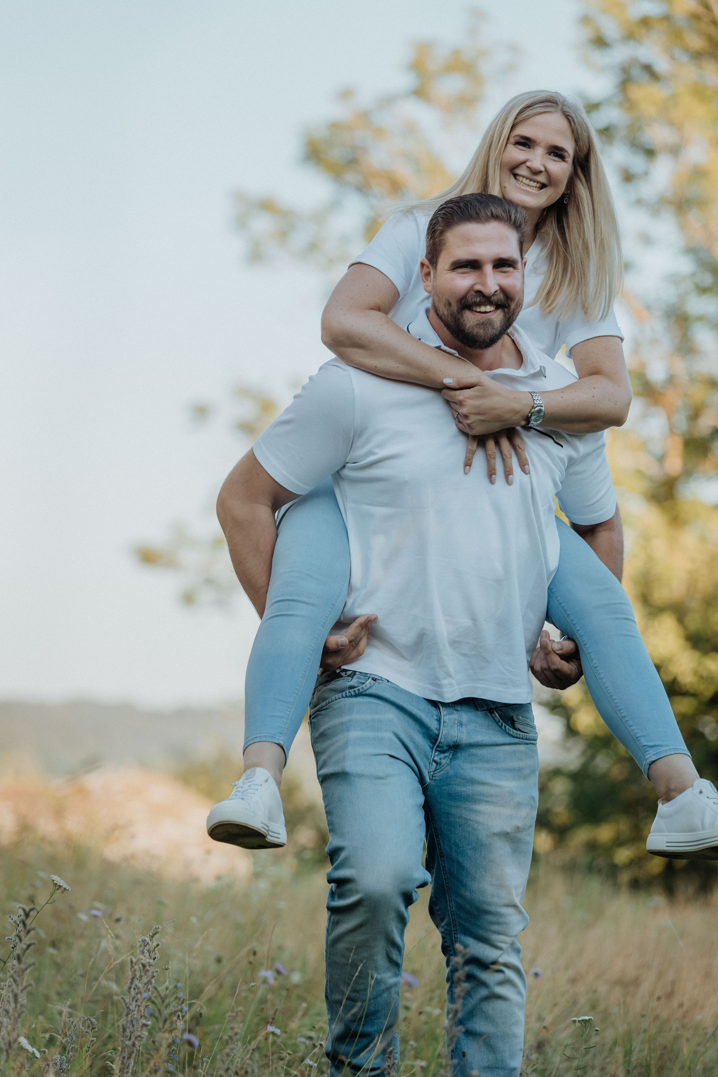 Couple in coordinated blue and white outfits playing and laughing in a grassy field.
