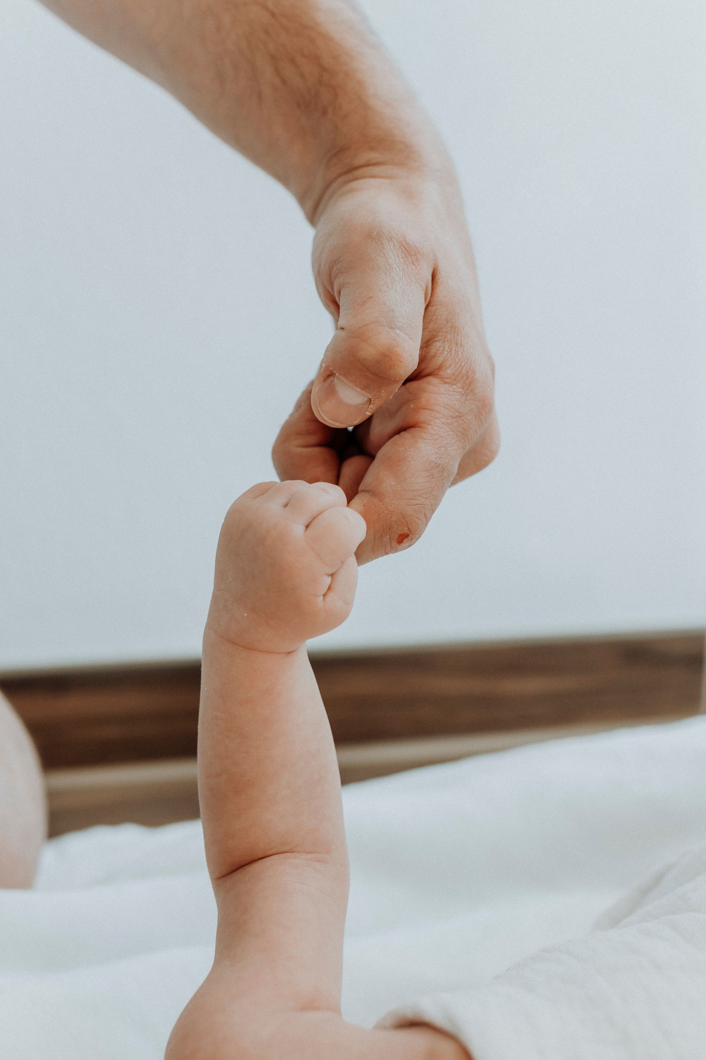 Close-up of tiny baby fingers grasping an adult's finger against white background.