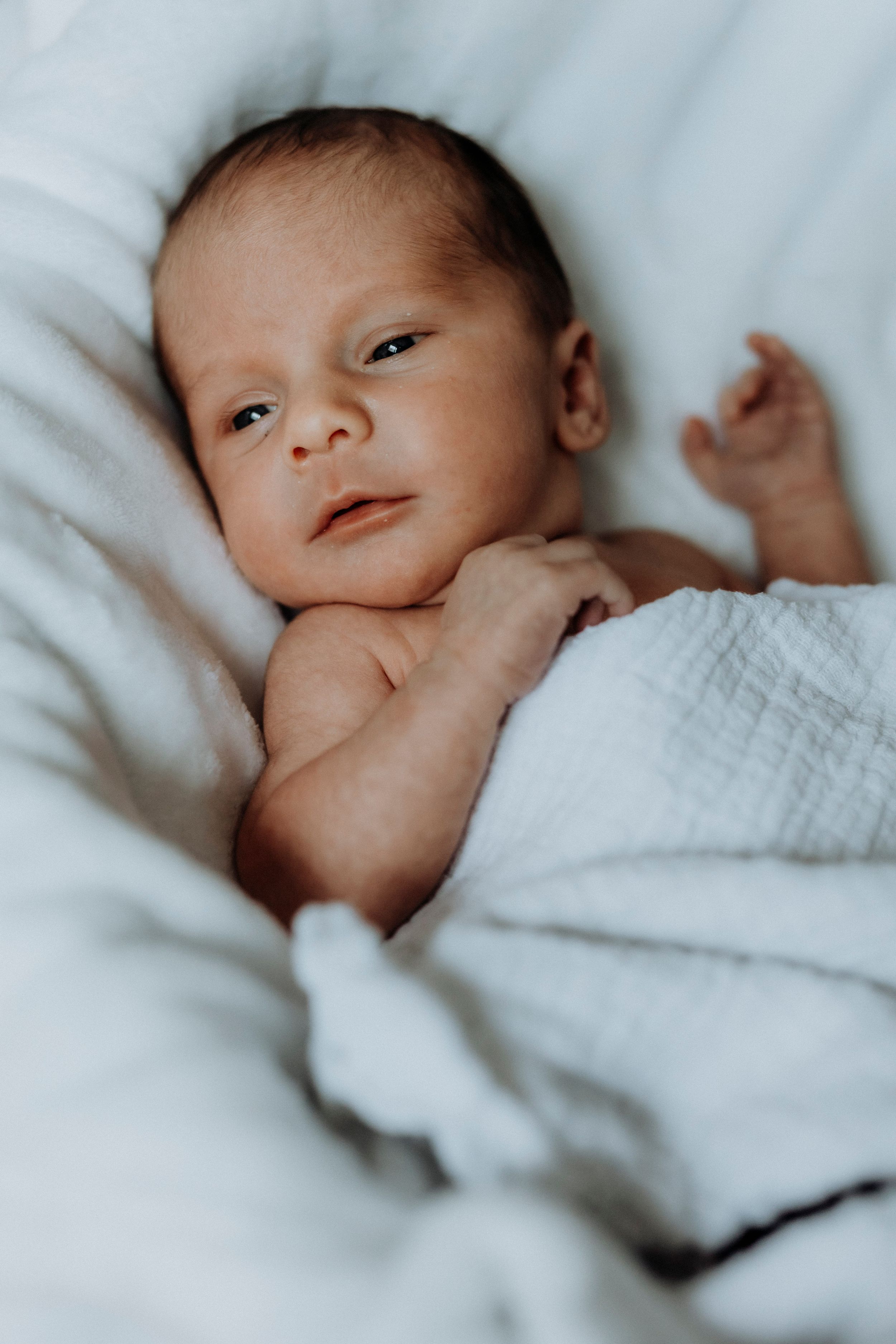 Close-up portrait of alert newborn baby wrapped in white textured blanket.