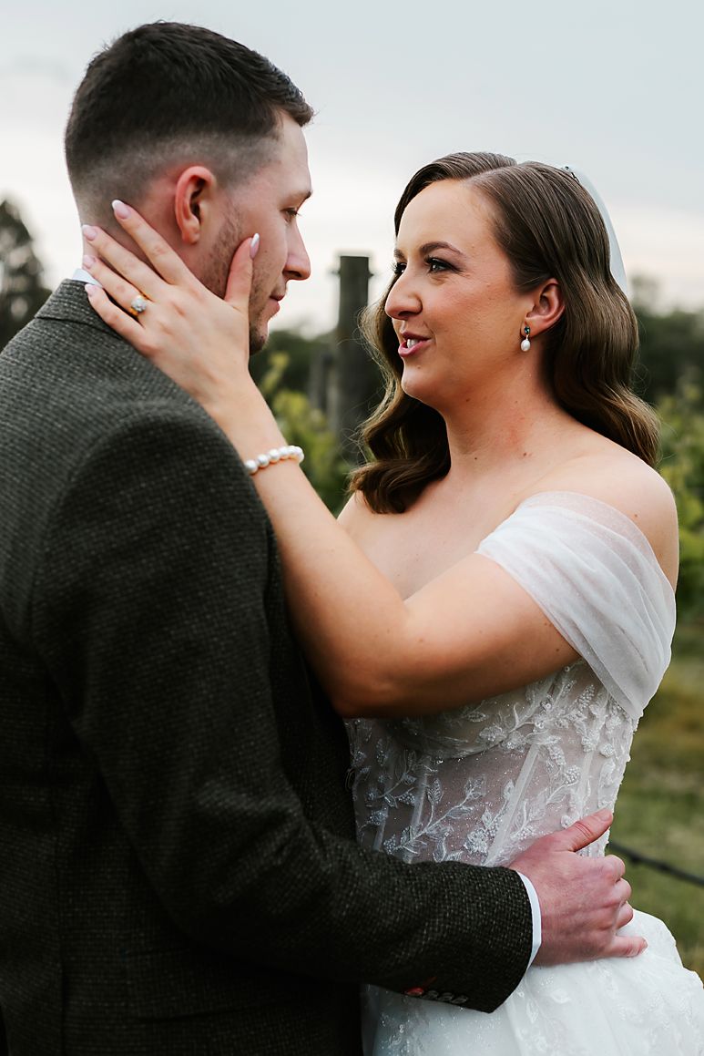 A romantic wedding moment captured outdoors as a couple embraces tenderly in formal attire.