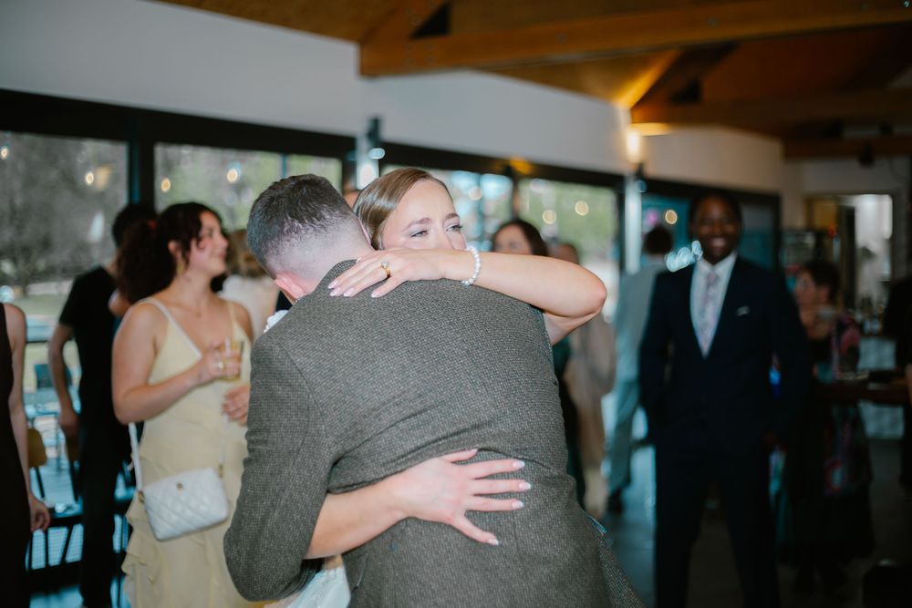 Wedding guests share emotional embraces and hugs during a reception celebration in a rustic venue.