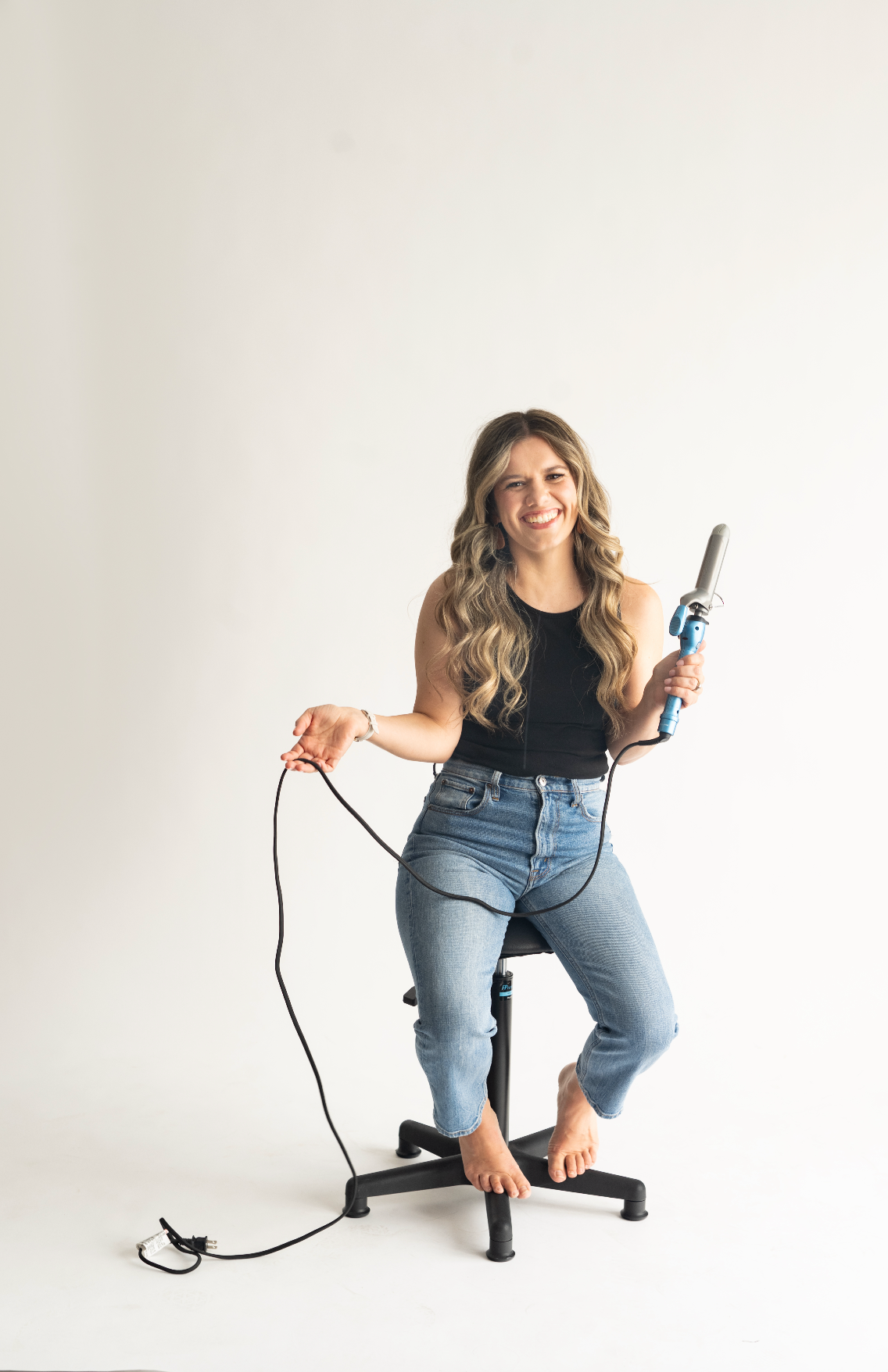 Woman in black top and jeans demonstrates jump rope exercise sequence against white background.