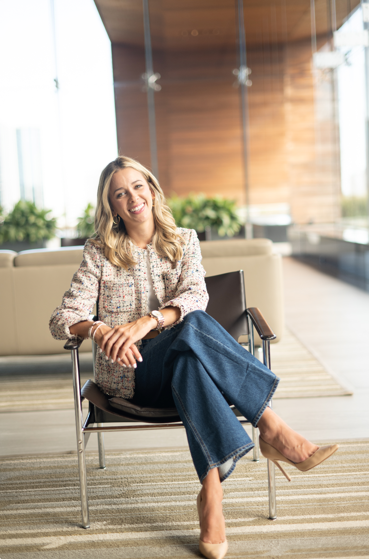 Professional wearing floral blouse and jeans relaxes in modern office chair with natural lighting.