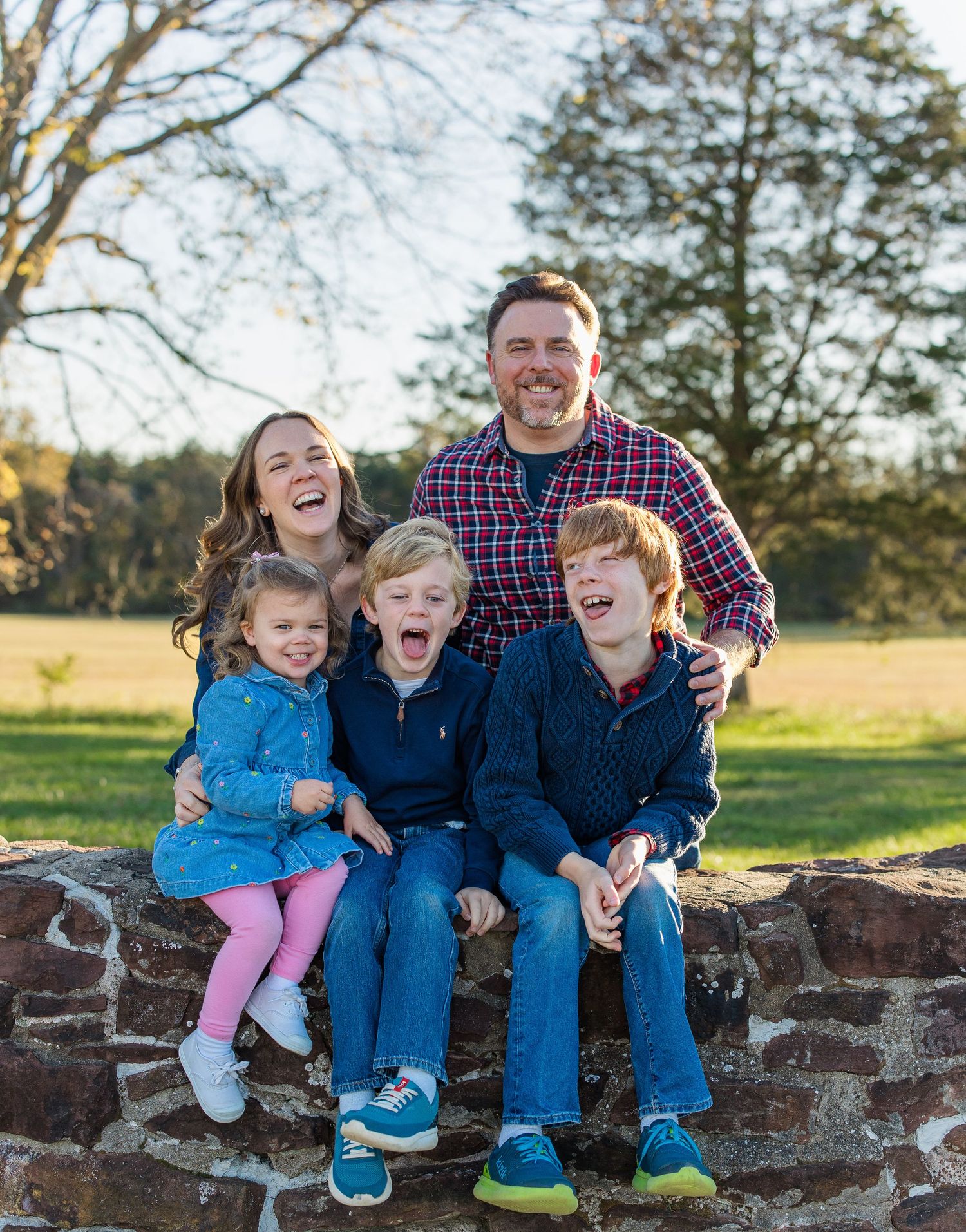 A family sits together on a stone wall outdoors, sharing joyful laughter and smiles in a series of candid moments.