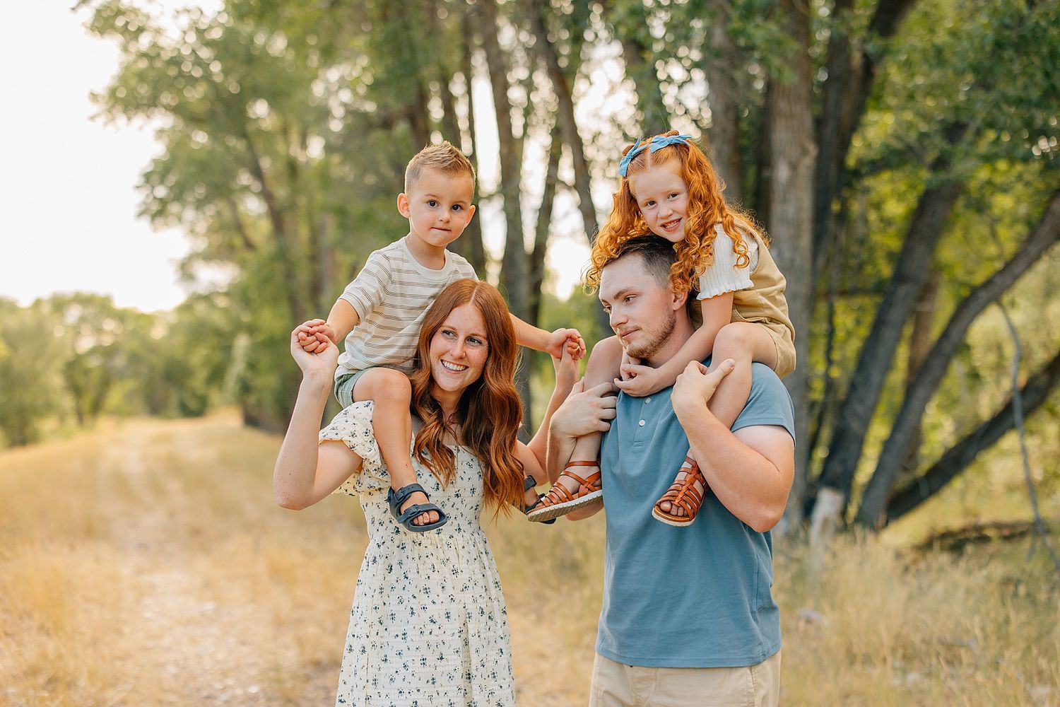 Joyful family enjoying a playful moment together in a sunlit outdoor setting with golden grass and trees.