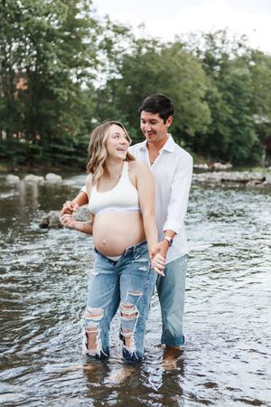 A couple shares playful moments while standing in shallow water wearing casual denim and white clothing.