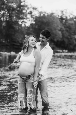 Playful couple splashing and laughing together in shallow water wearing casual clothes.
