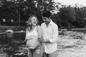 A couple shares tender moments by a stream in black and white maternity photos.