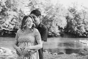 Romantic outdoor maternity photoshoot near a serene river with natural greenery in the background.