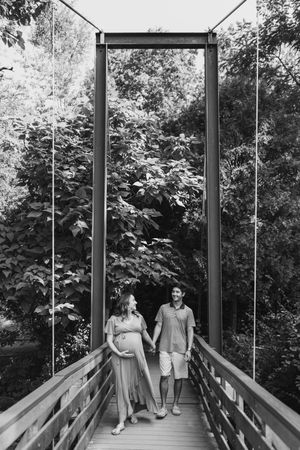 Black and white series captures couple walking together on elevated wooden boardwalk surrounded by trees.