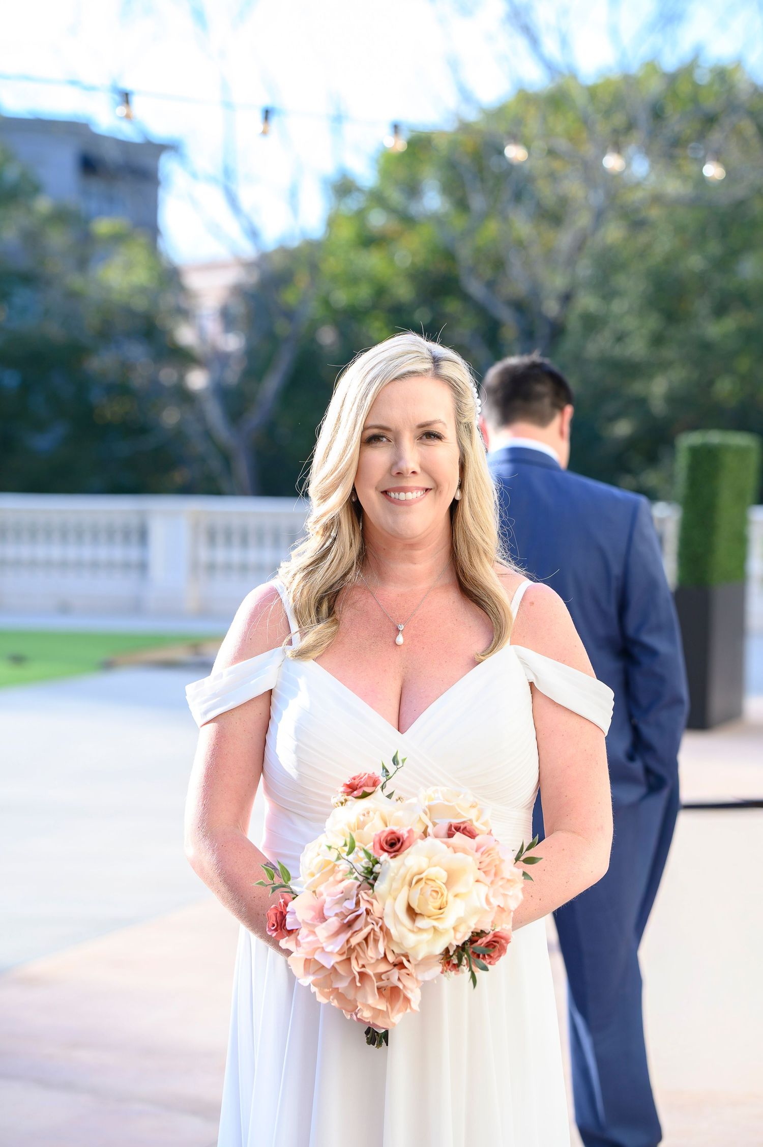 Bride in white wedding dress holds a peach and pink floral bouquet during an outdoor ceremony. wedding photos in alpharetta, GA