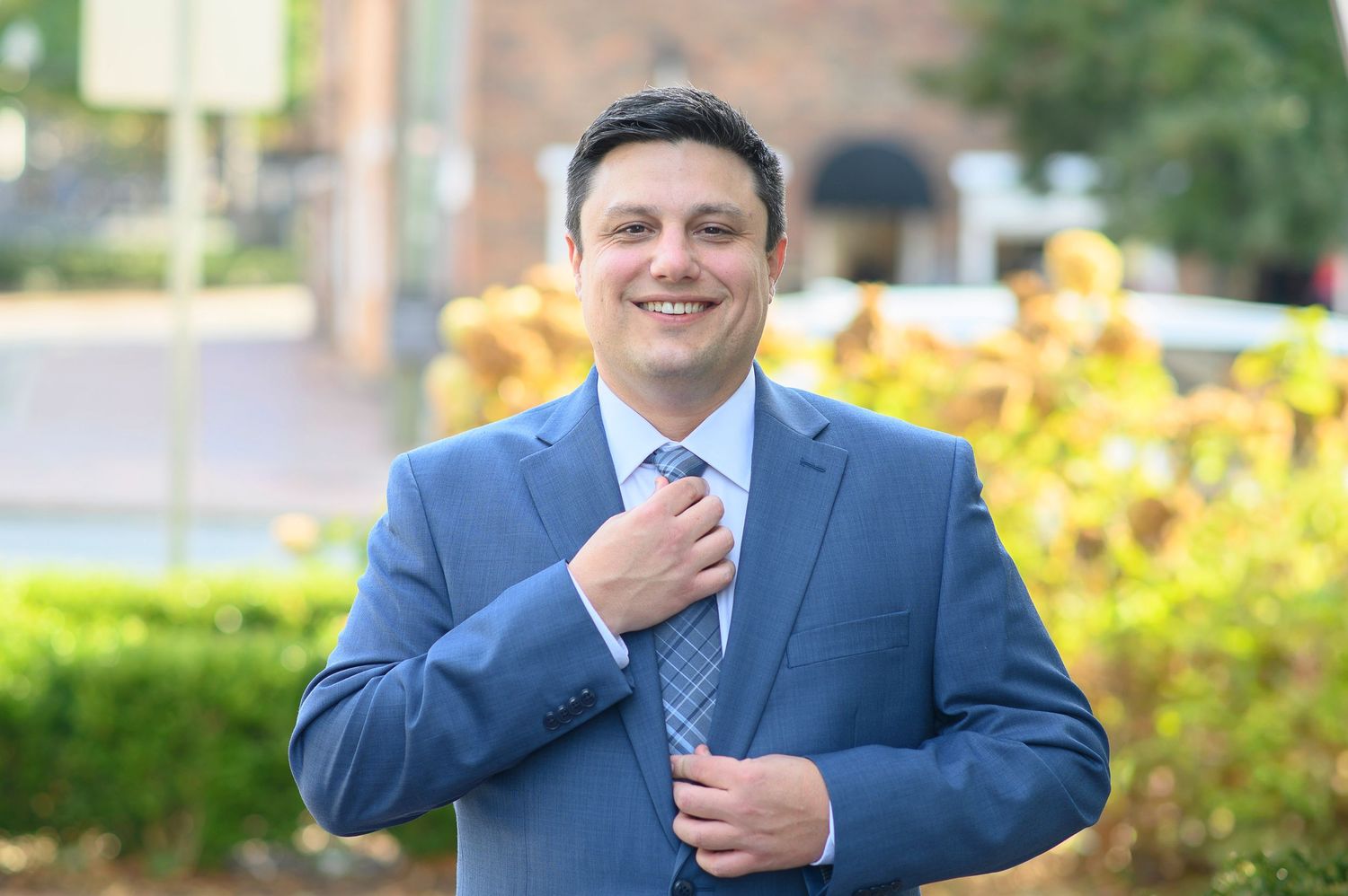 groom in a navy blue suit adjusts his tie while standing outdoors with yellow flowers in the background. wedding photos in alpharetta, GA