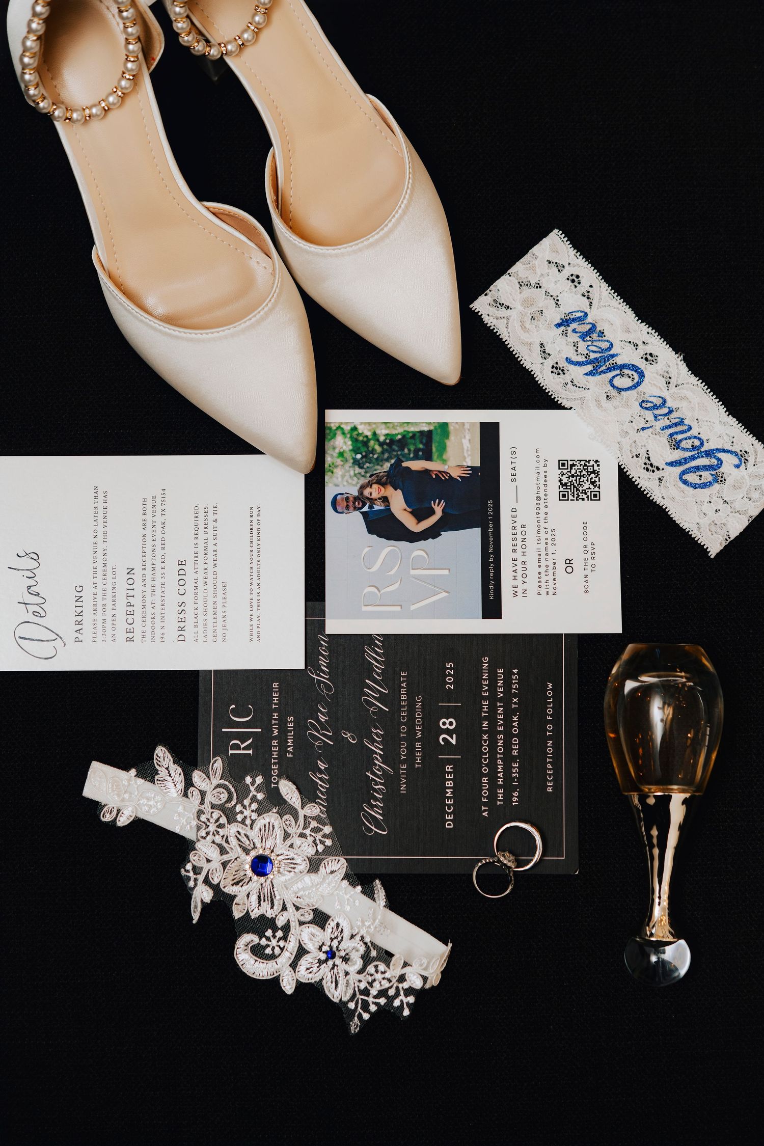 Elegant wedding details including white heels, invitations, jewelry, and garter laid out on black background.