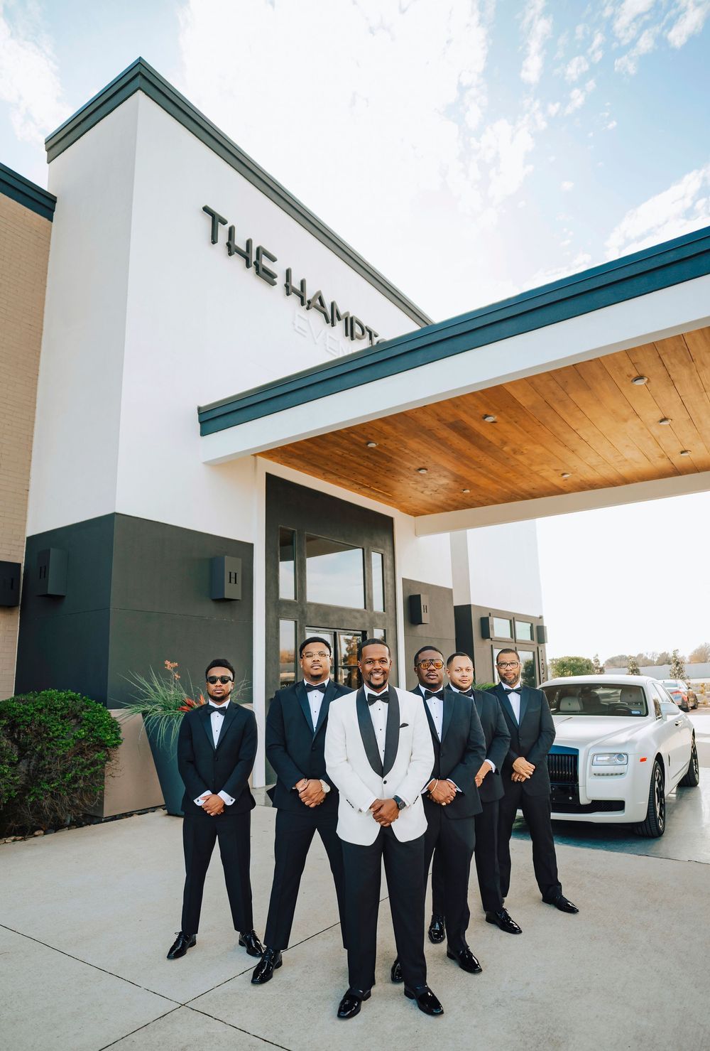 Groomsmen in dark suits pose together outside a modern building.